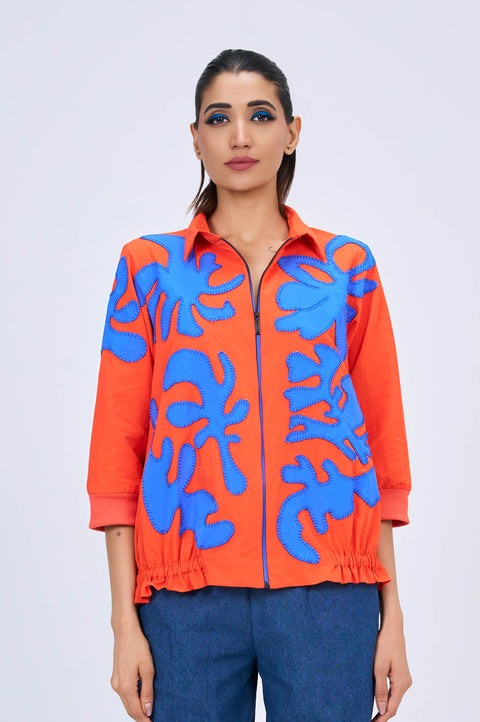 Flame orange zip-front shirt for women with blue appliqué and gathered hem, front view